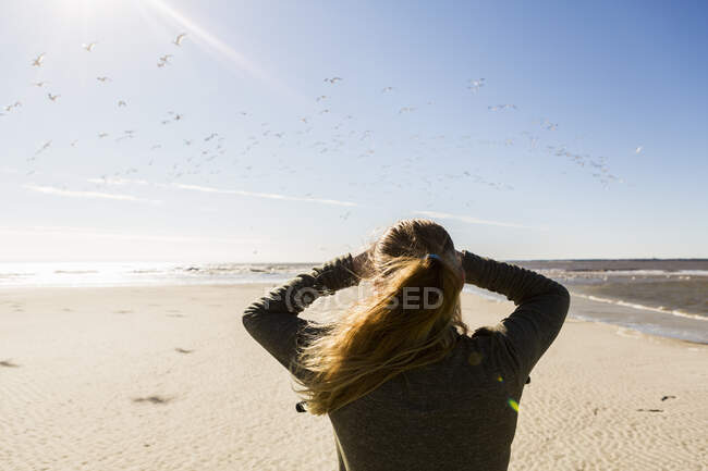 Девочка-подросток, стоящая на широком открытом пляже, глядя вдаль. — стоковое фото