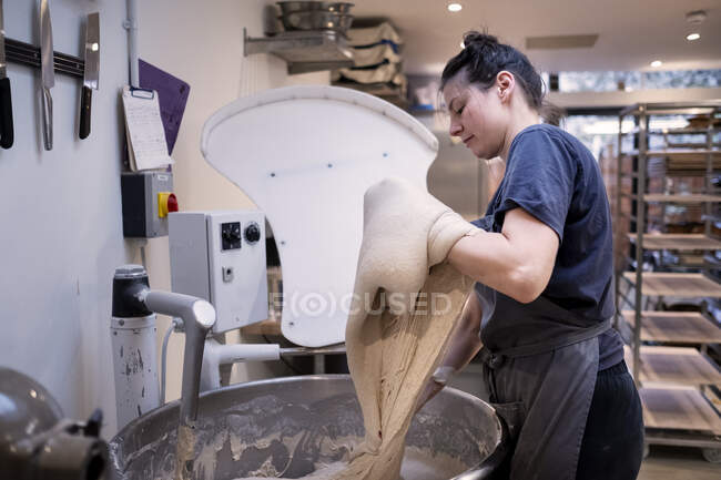 Woman wearing apron standing in an artisan bakery, working with sourdough. — Stock Photo