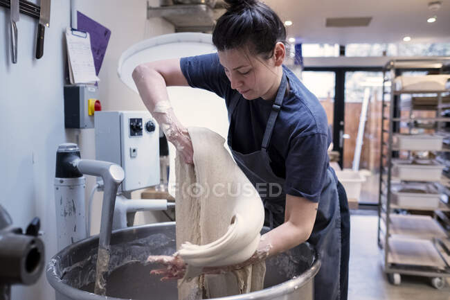 Frau mit Schürze steht in einer Bäckerei und arbeitet mit Sauerteig. — Stockfoto