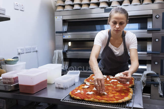 Frau mit Schürze steht in Bäckerei und bereitet Pizza zu. — Stockfoto