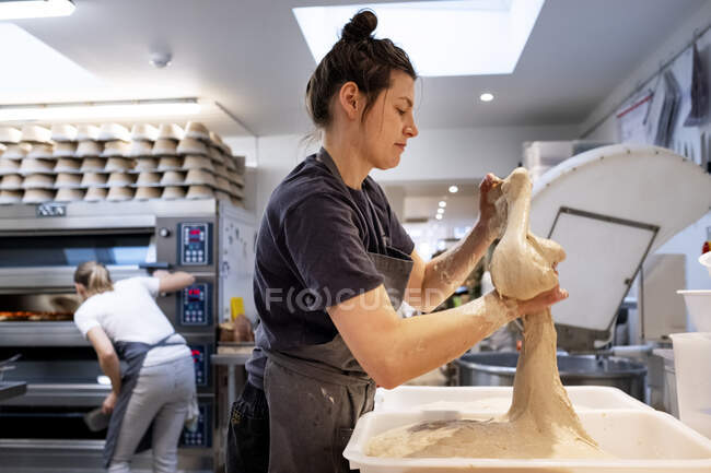 Mulher vestindo avental de pé em uma padaria artesanal, trabalhando com massa . — Fotografia de Stock