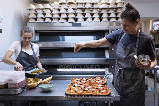 Frauen mit Schürze stehen in einer Bäckerei und bereiten Pizza zu. — Stockfoto