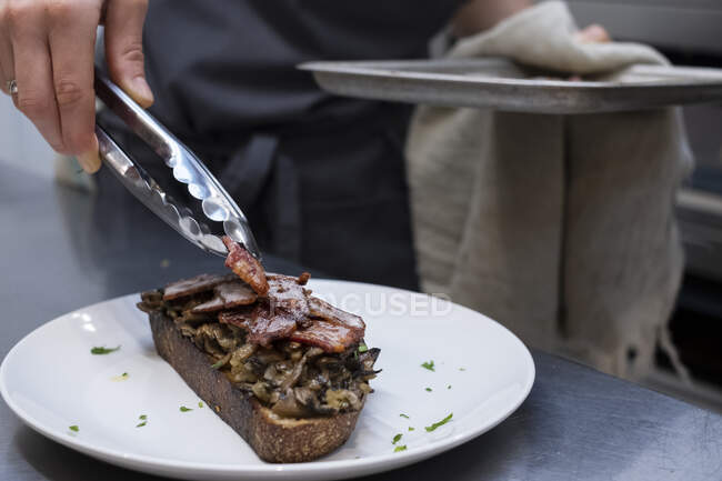 High angle close up of chef preparing toasted bread with bacon and mushrooms in an artisan bakery. — Stock Photo