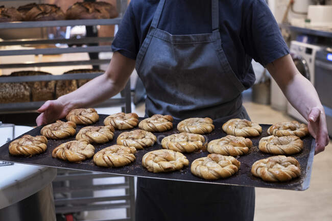 Закрыть лицо, держащее поднос со свежеиспечёнными булочками с корицей в пекарне . — стоковое фото