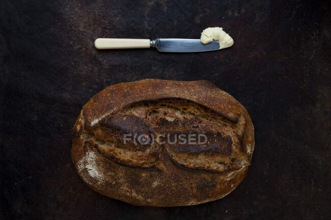 Pan recién horneado en una panadería artesanal con un cuchillo y una porción de mantequilla
. - foto de stock