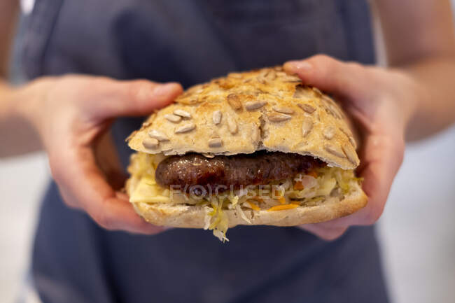 Close up of a person holding freshly made sausage bap, a seeded bun in an artisan bakery. — Stock Photo