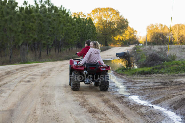 Two teenagers riding on a buggy, all terrain vehicle on a muddy track. — Stock Photo