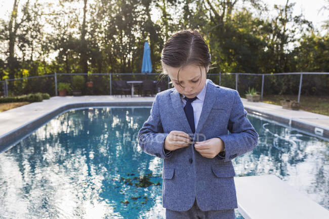6 anno vecchio ragazzo abbottonatura suo vestito con piscina in background — Foto stock