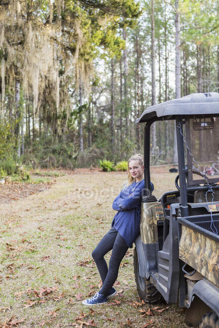 A teenage girl by an all terrain vehicle, a buggy, leaning with arms folded. — Stock Photo