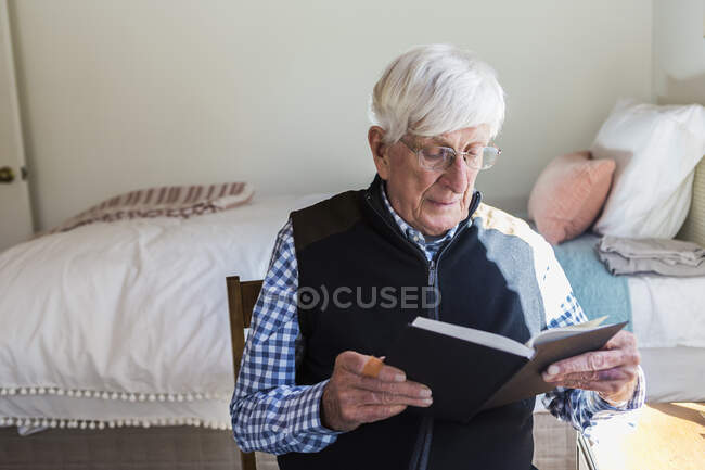Hombre mayor leyendo un libro en su dormitorio - foto de stock