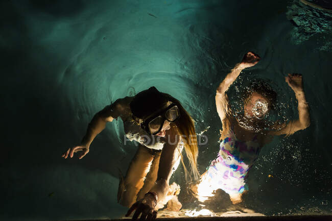 Dos niños nadando en la piscina por la noche - foto de stock