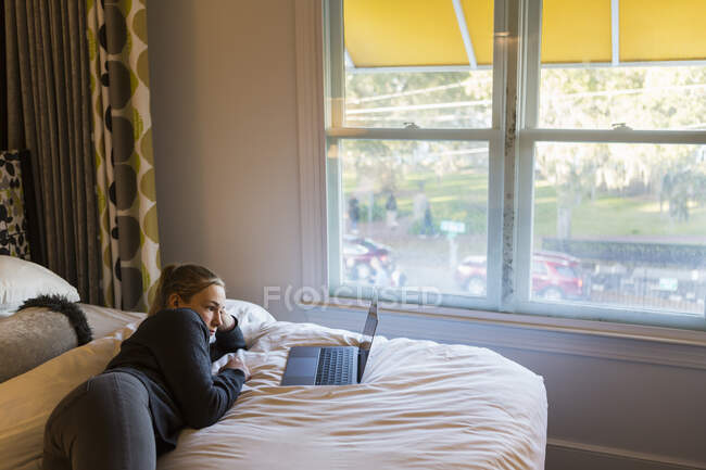 13-летняя девочка лежит на кровати и смотрит на свой ноутбук — стоковое фото
