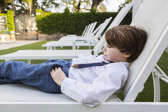 Niño de 6 años reclinado en silla de jardín - foto de stock