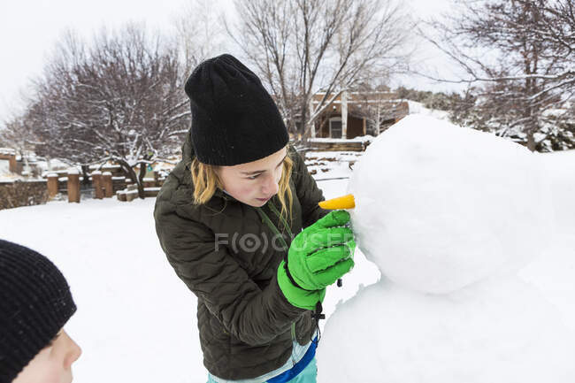 Ragazza adolescente e suo fratello minore costruiscono un pupazzo di neve in un giardino — Foto stock