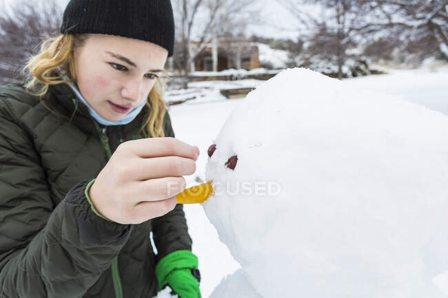 Teenage girl building a snowman adding nose and eyes — Stock Photo