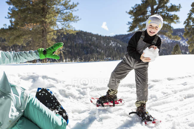 Garçon de six ans avec des raquettes tenant une grosse boule de neige . — Photo de stock
