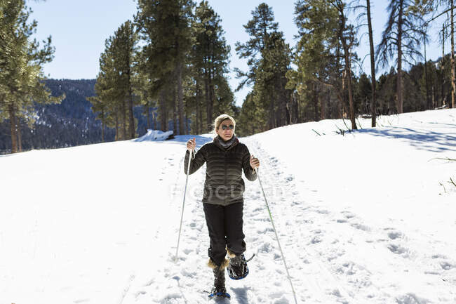 Donna adulta che indossa le racchette da neve con bastoncini su un sentiero . — Foto stock