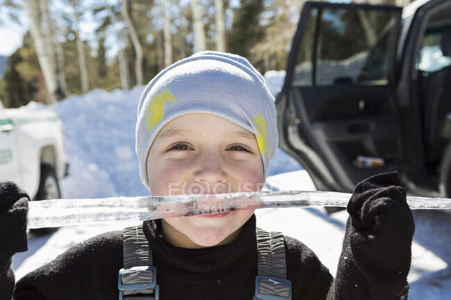 Smiling six year old boy with a long icicle in his mouth — Stock Photo