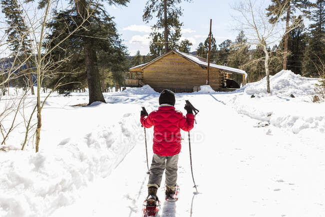 Rear view of young boy in a red jacket snow shoeing — Stock Photo