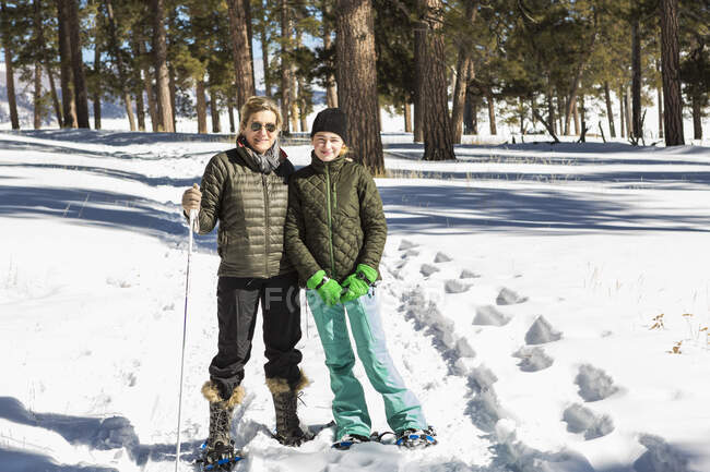 Mujer adulta y adolescente en zapatos de nieve en bosques sosteniendo bastones de esquí - foto de stock