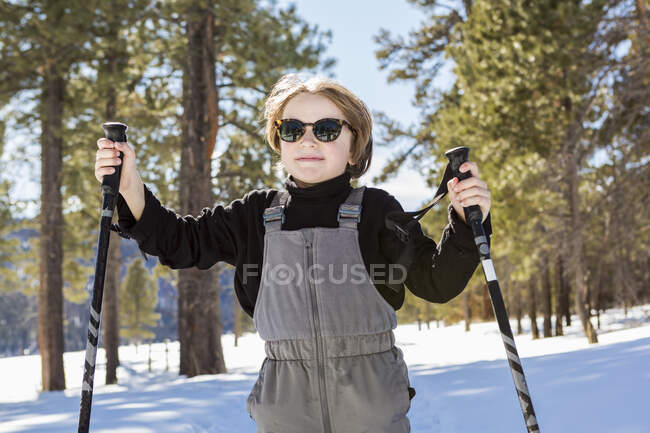 Garçon de six ans en forêt tenant des bâtons de ski — Photo de stock
