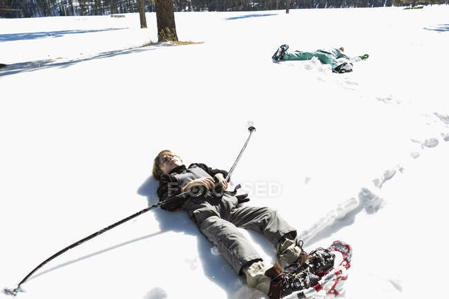 Six year old boy wearing snow shoes, lying down on his back in snow — Stock Photo