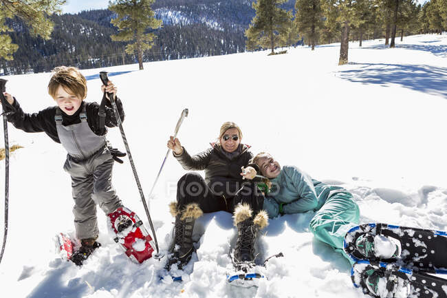 Una mujer y dos niños en raquetas de nieve en la nieve gruesa, madre e hija tumbadas en el suelo riendo . - foto de stock