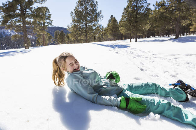 Дівчина-підліток в снігових туфлях лежить на снігу сміється — стокове фото