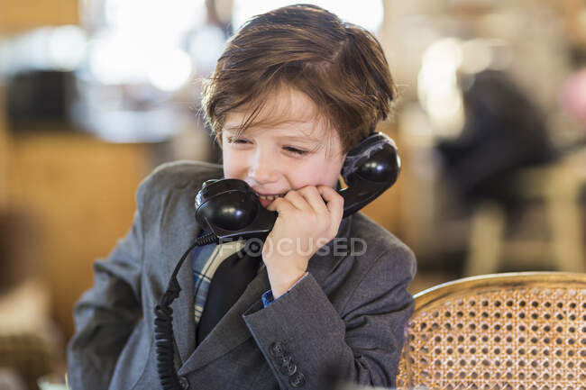 Шість років хлопчик у костюмі розмовляє на старовинному телефоні вдома — стокове фото