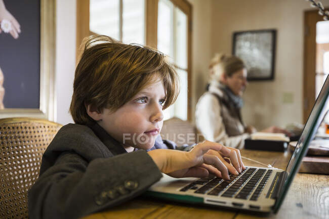 Focalizzato ragazzo di sei anni digitando su un computer portatile a casa — Foto stock