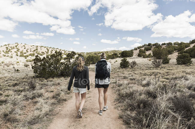 Vista trasera de la mujer adulta y su hija adolescente de senderismo en la cuenca del Galisteo, NM. - foto de stock