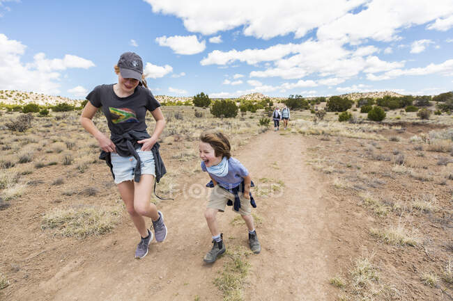 Niño de 6 años corriendo en sendero con su hermana mayor, Cuenca Galisteo, NM. - foto de stock