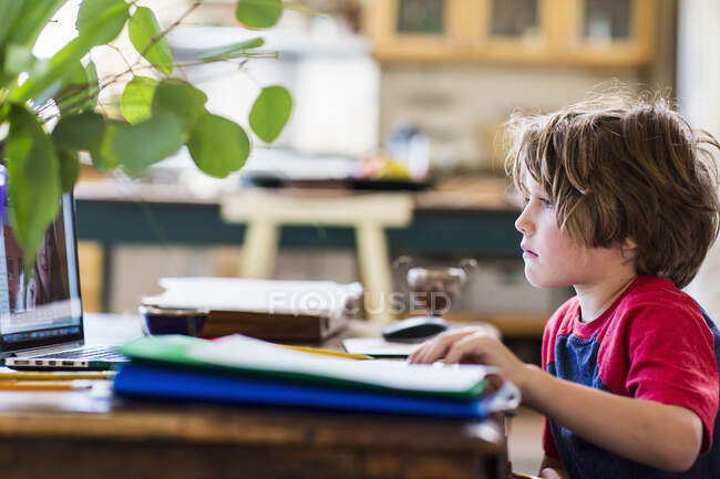 Un niño que trabaja en casa, mirando una pantalla en línea lecciones, la educación en el hogar, durante un encierro - foto de stock
