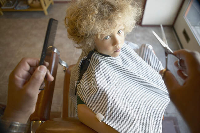 Барбер тягнеться, щоб підстригти хлопчаче волосся. — стокове фото