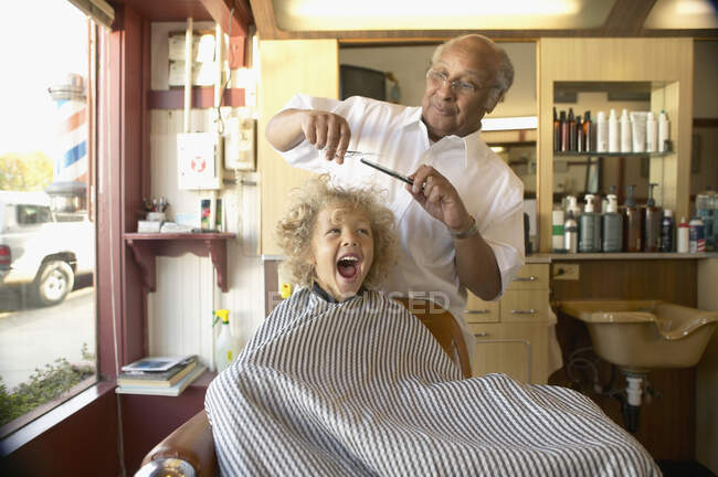 Jeune garçon criant tandis que le coiffeur se coupe les cheveux — Photo de stock