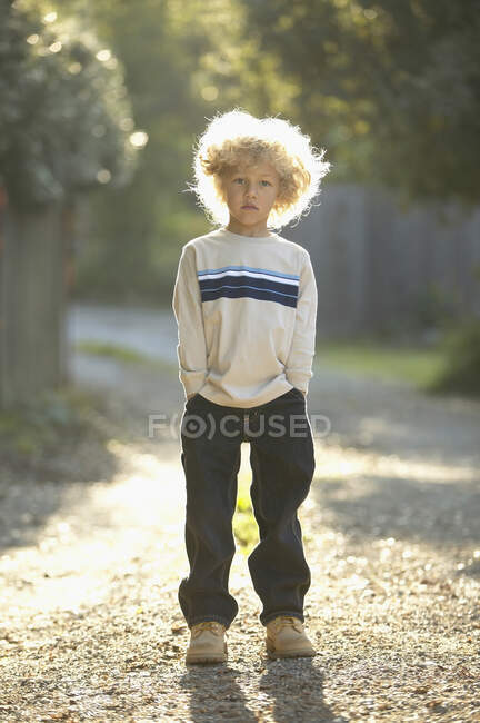 Мальчик стоит на гравийной дорожке, руки в карманах. — стоковое фото