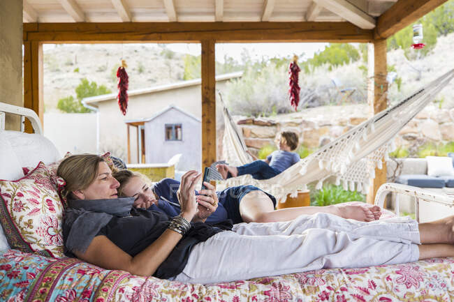 Mère et fille couchées ensemble sur un lit extérieur regardant un écran de téléphone intelligent — Photo de stock