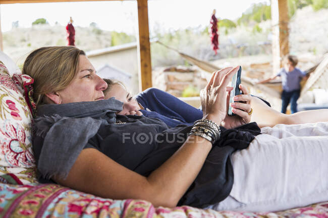 Mother and daughter lying together on an outdoor bed looking at a smart phone screen — Stock Photo