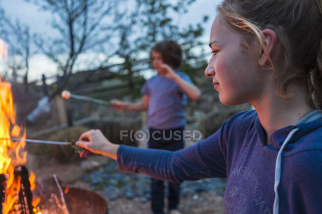 Adolescente faire des smores avec son frère sur un feu dans un jardin au crépuscule. — Photo de stock