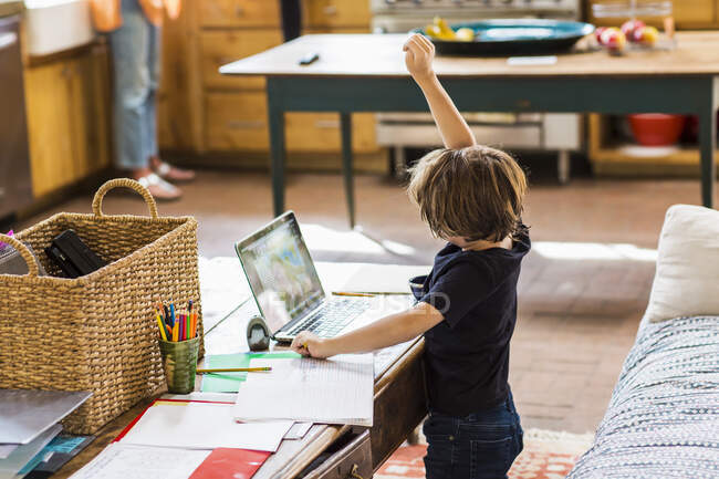 Дитина працює вдома, дивлячись на вчителя на екрані онлайн уроки, піднімаючи руку, щоб відповісти на питання — стокове фото