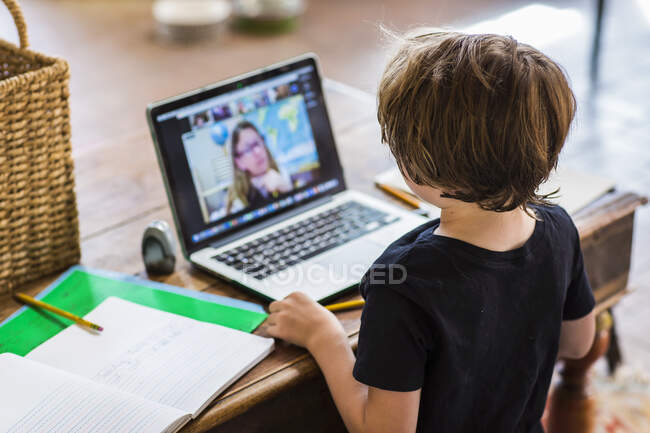 Uma criança trabalhando em casa, olhando para o professor na tela aulas on-line durante o confinamento — Fotografia de Stock