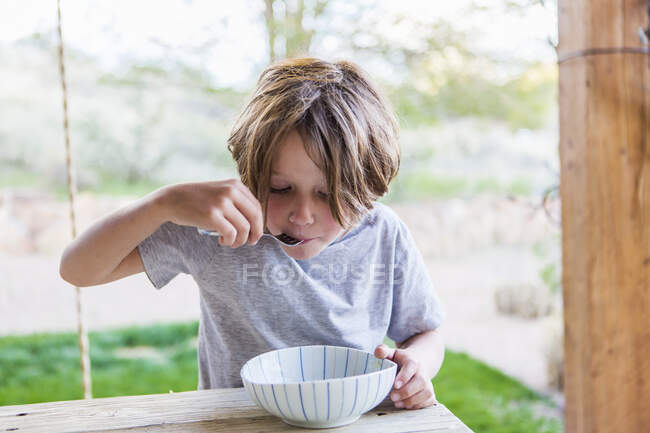 6 anno vecchio ragazzo mangiare riso su suo patio — Foto stock