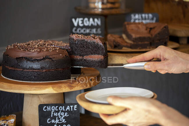 Close up of waitress putting slice of chocolate fudge cake on a plate door of a cafe. — Stock Photo