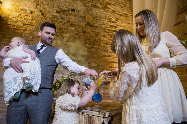 Famiglia che versa sabbia colorata nel barattolo di vetro durante la cerimonia di nomina in un fienile storico. — Foto stock