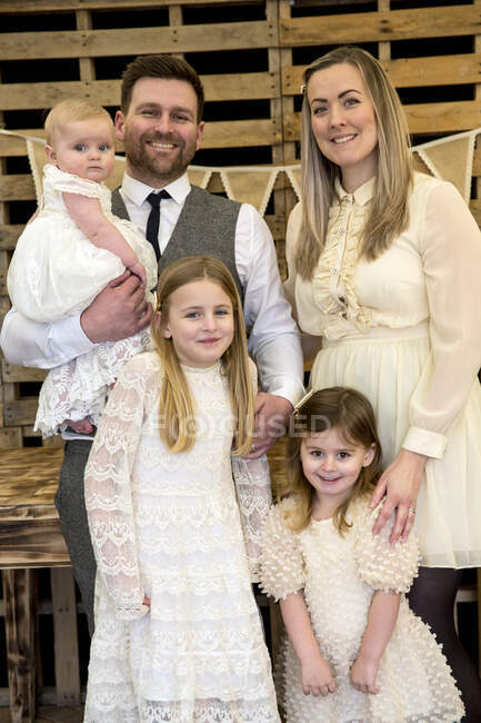 Porträt lächelnder Eltern mit ihren drei kleinen Töchtern bei der Taufzeremonie in einer historischen Scheune. — Stockfoto