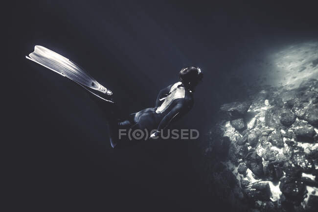 Unterwasser-Ansicht eines Tauchers mit Neoprenanzug und Schwimmflossen, der in der Nähe von Felsen taucht. — Stockfoto