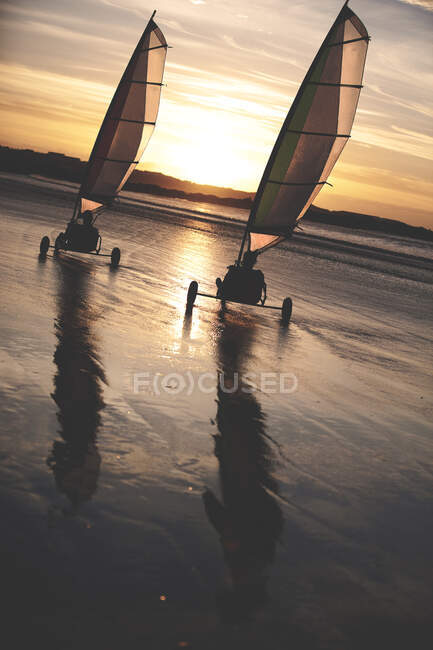 Two sand yachts racing along a sandy beach at sunset. — Stock Photo