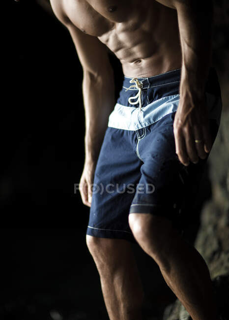 Low section of man with muscular build wearing blue swimming trunks. — Stock Photo