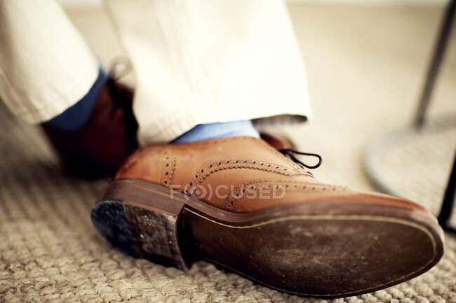 Primo piano dei piedi della persona, con spille di pelle marrone, calzini blu e pantaloni bianchi. — Foto stock