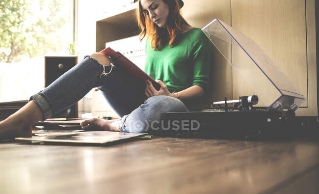 Mulher sentada no chão ao lado de um gira-discos olhando para uma manga recorde. — Fotografia de Stock